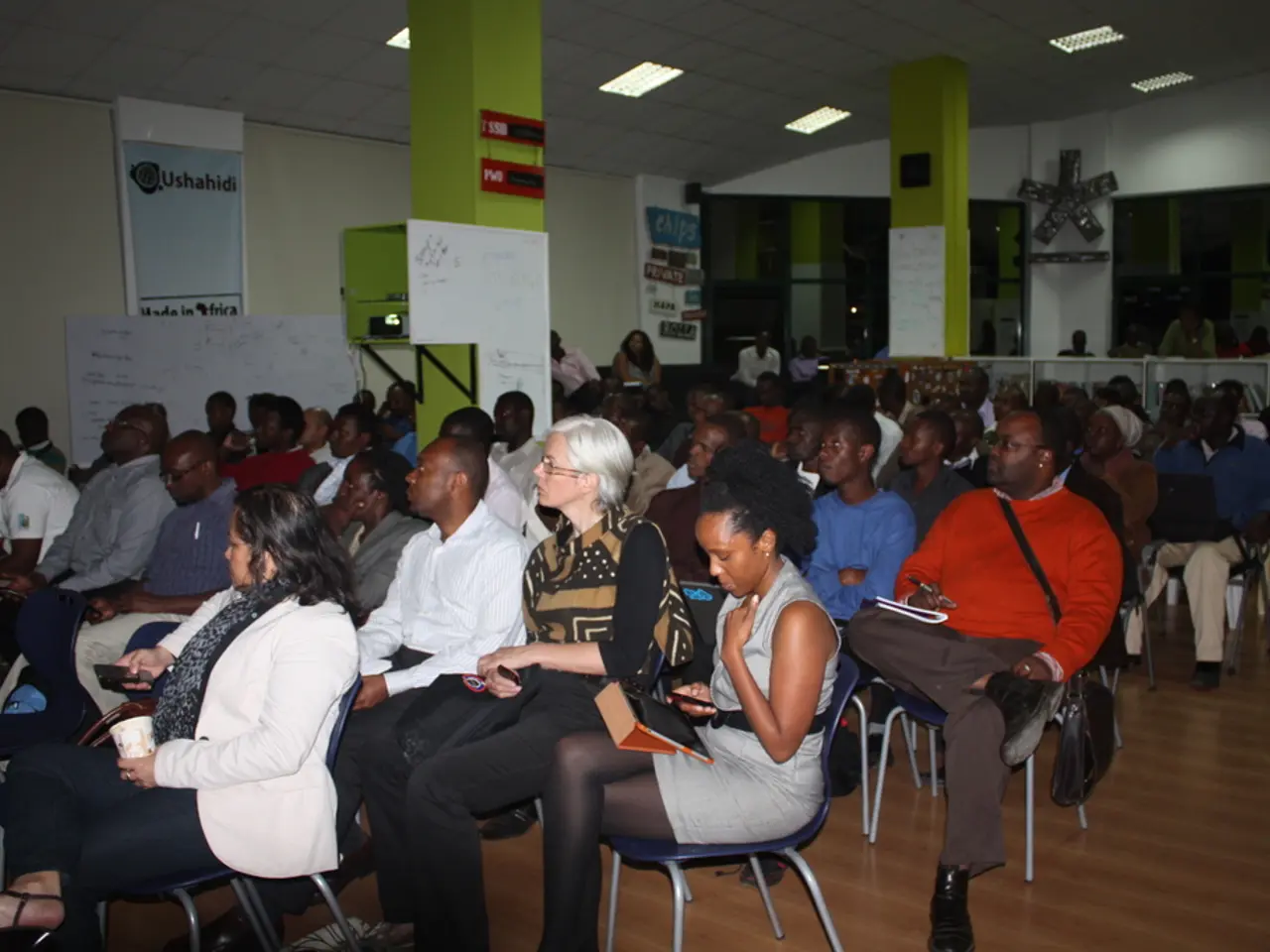 It looks like a classroom,there are many people sitting on the chairs there are two green color...
