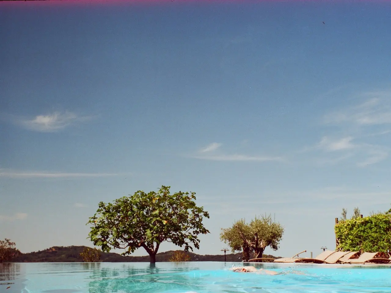 In this image we can see a person swimming in a pool. We can also see some benches, a group of...