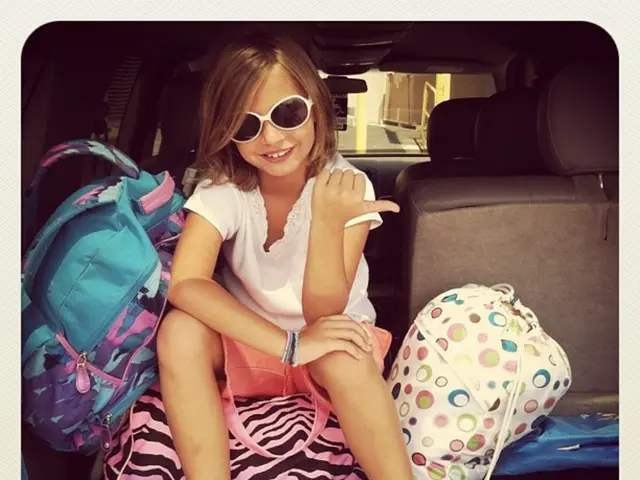 As we can see in the image there is a girl wearing spectacles and sitting on bag and there is a...